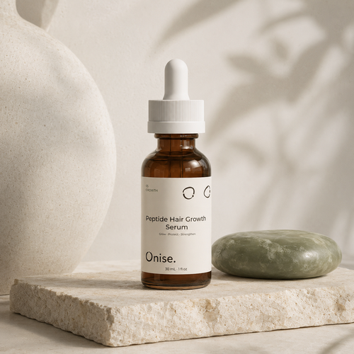An amber glass dropper bottle labeled 'Onise. Peptide Hair Growth Serum' stands on a light stone slab beside a green soap bar, with a large textured vase and soft shadowy leaves in the background.