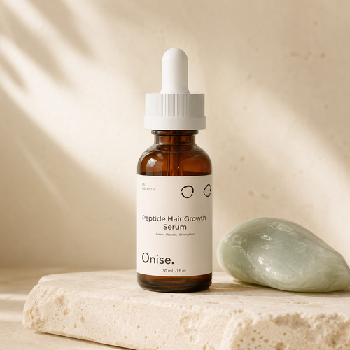 An amber glass dropper bottle labeled Onise Peptide Hair Growth Serum stands on a light stone slab next to a pale green polished stone, with soft warm shadows on a beige background.